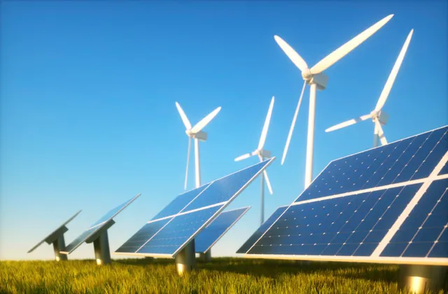 Solar panels and wind turbines in a meadow under a clear sky